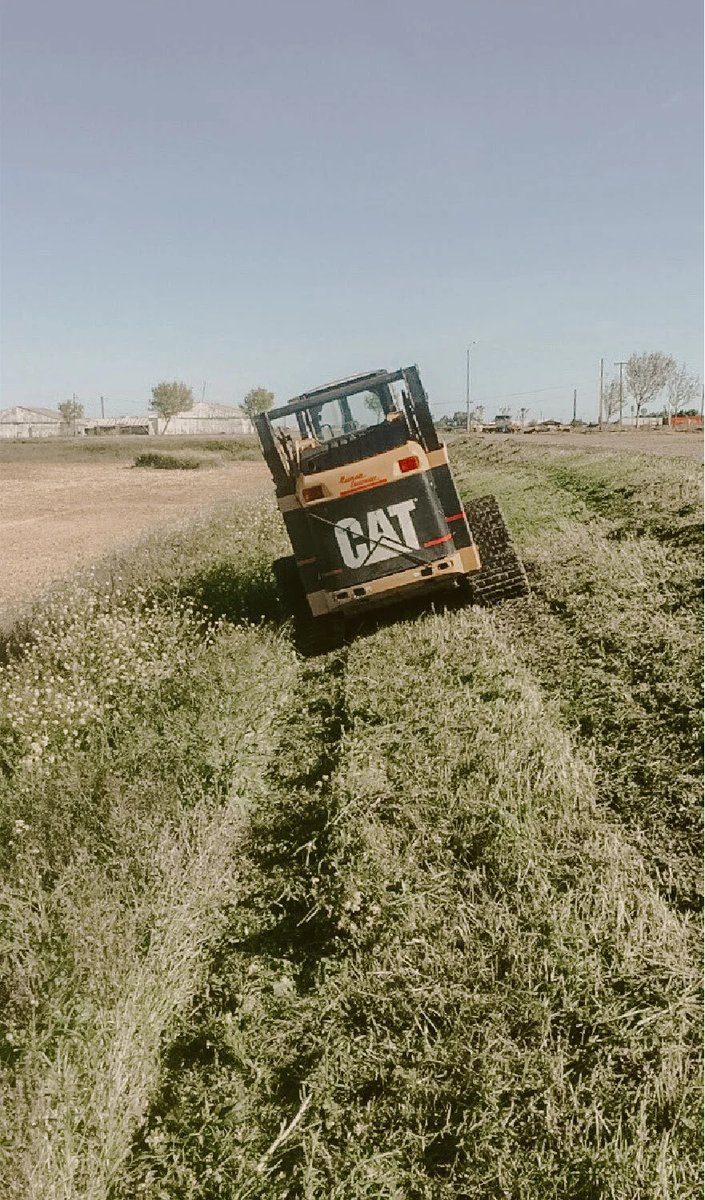 Yellow skid steer with mower attachment cutting a grassy slope