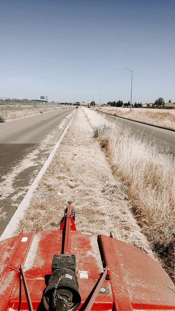 Mower deck clearing dry grass along the shoulder of a paved road